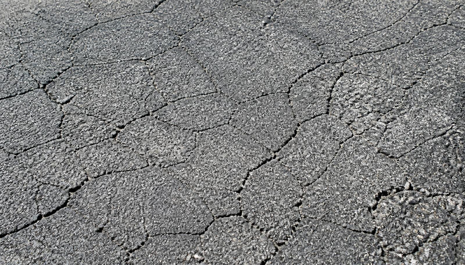 Sun-faded gray asphalt with hairline spiderweb cracking caused by UV oxidation in Central Valley heat.