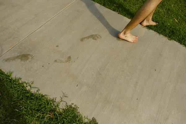 Barefoot person walking across a clean custom concrete sidewalk in California with visible wet footprints.