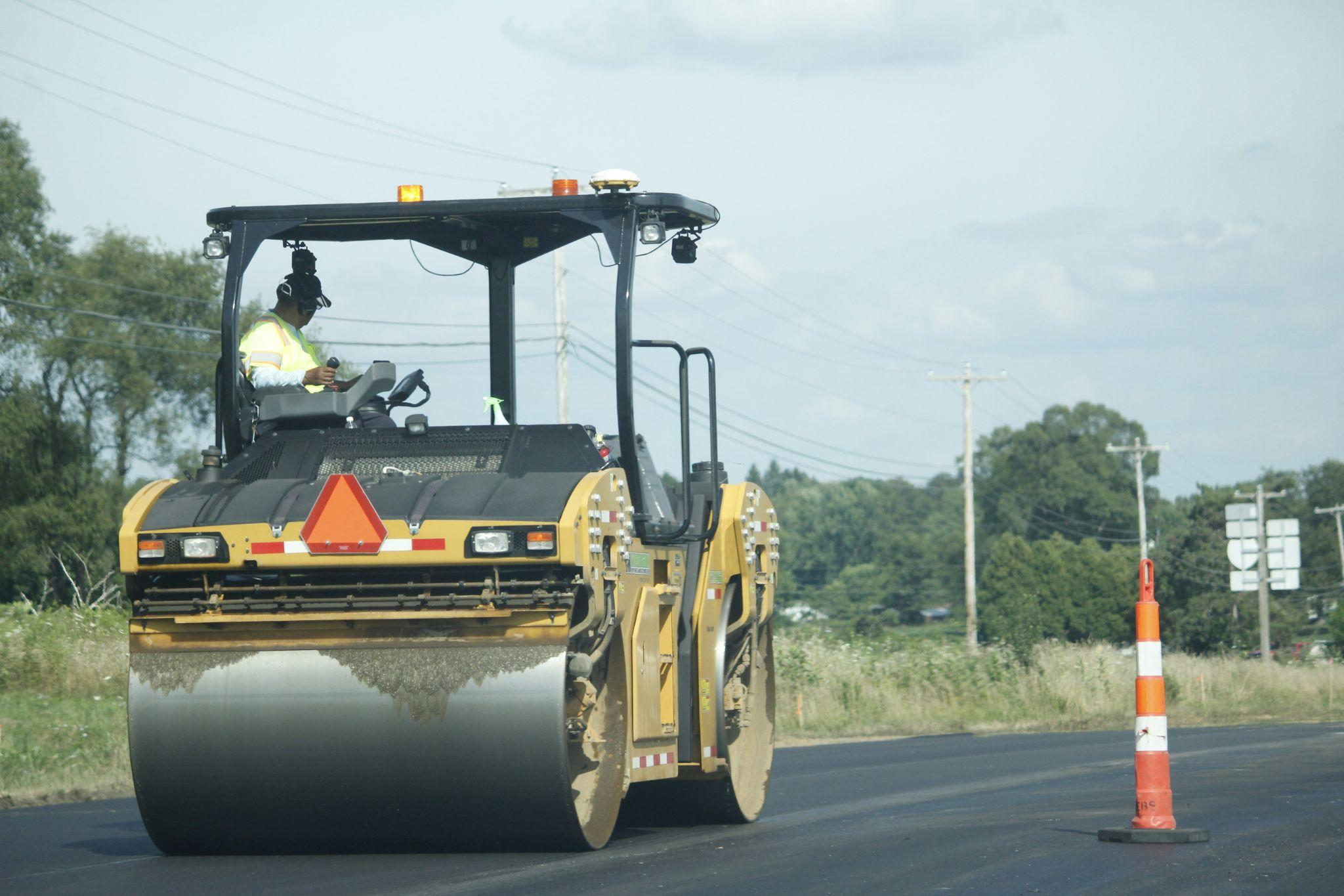 Workers operate paving equipment for asphalt road paving in California.