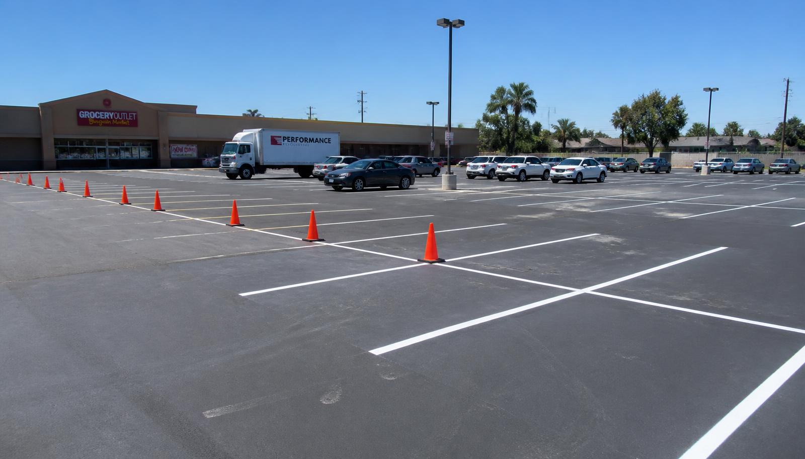 Freshly repaved commercial parking lot in Fresno with new white striping and cones sectioning off a phased work area while customers still park