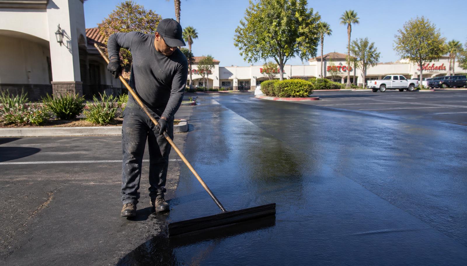 Technician applying asphalt sealcoating in a California shopping center parking lot